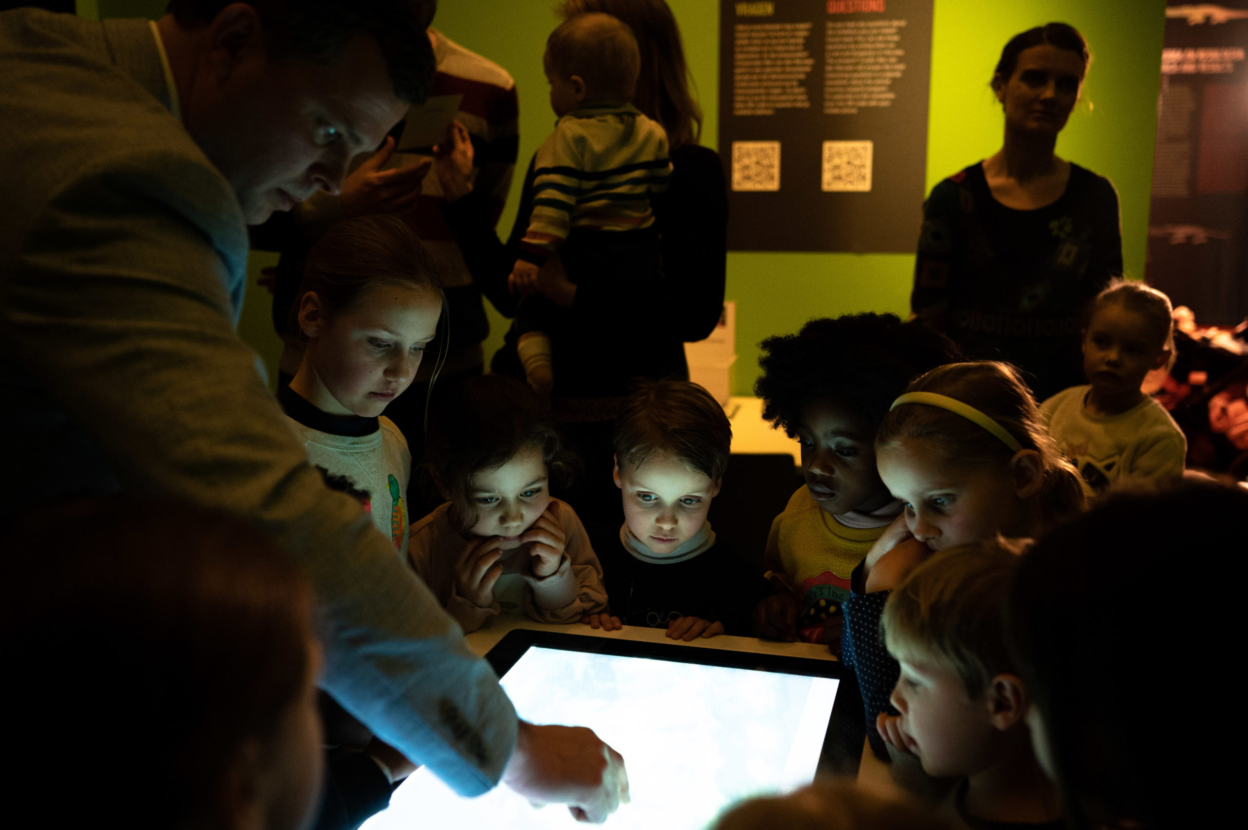 Een groep jonge kinderen kijkt naar een scherm in een tentoonstellingszaal. 